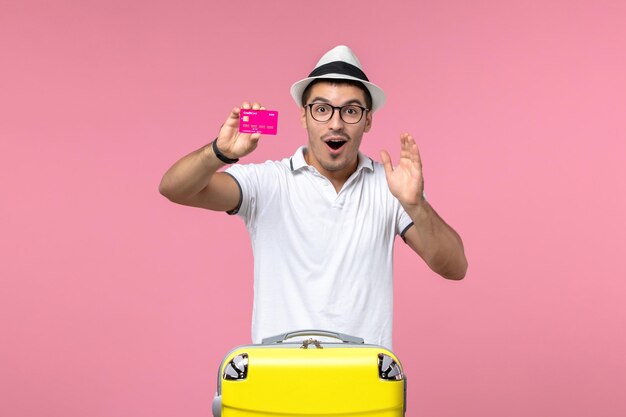 Вид спереди молодого человека, держащего банковскую карту на розовой стене