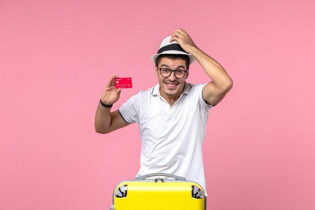 Front view of young man holding bank card and smiling on pink wall