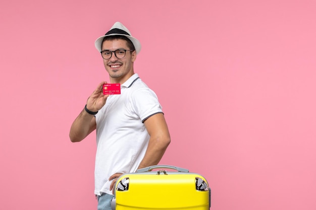 Front view of young man holding bank card and smiling on the pink wall