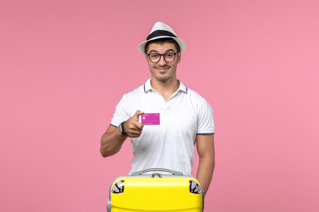 Вид спереди молодого человека, держащего банковскую карту на летних каникулах на светло-розовой стене