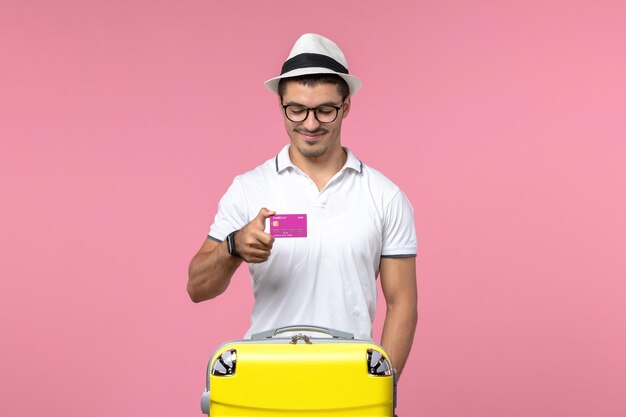 ピンクの壁に夏休みに銀行カードを保持している若い男の正面図