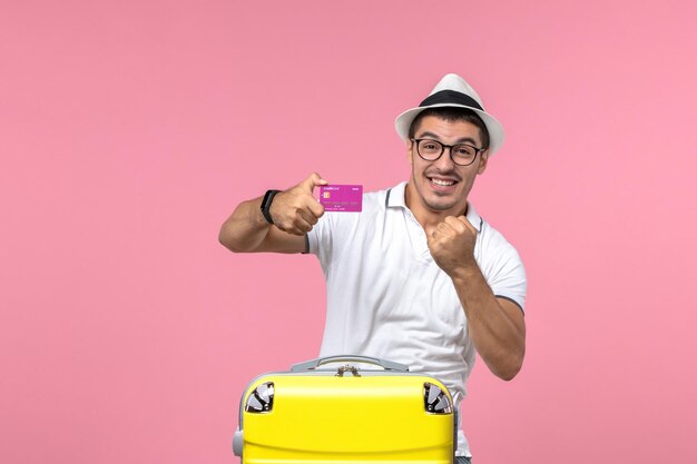 Вид спереди молодого человека, держащего банковскую карту на летних каникулах на розовой стене