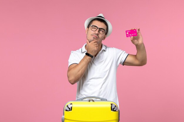 Front view of young man holding bank card on summer vacation on pink wall