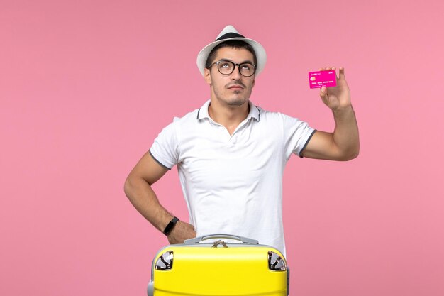 분홍색 벽에 여름 방학에 은행 카드를 들고 있는 젊은 남자의 전면 보기