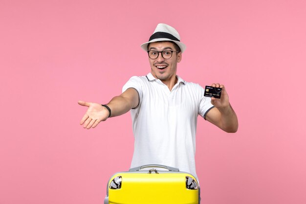 Front view of young man holding bank card on summer vacation on the pink wall