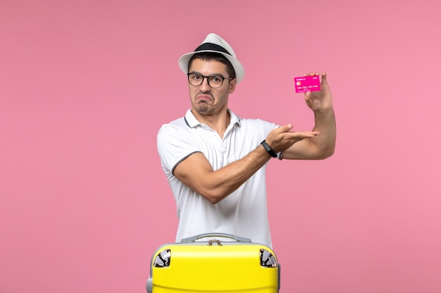 Front view of young man holding bank card on a vacation on pink wall