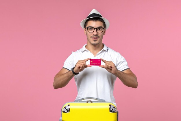 Front view of young man holding bank card on vacation on a pink wall