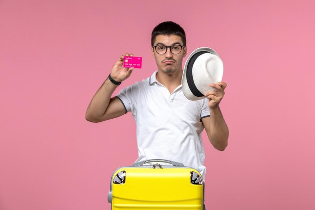 Вид спереди молодого человека, держащего банковскую карту в отпуске на розовой стене