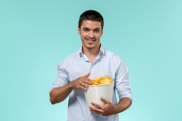 Front view young man holding basket with cips on the blue background film remote movie cinema theater