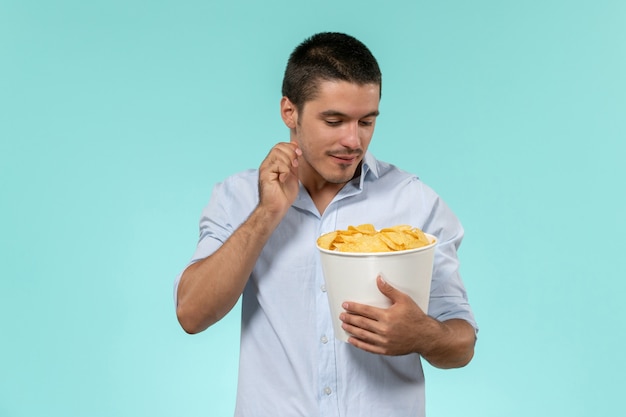 Front view young man holding basket with cips on blue wall film remote movie cinema male