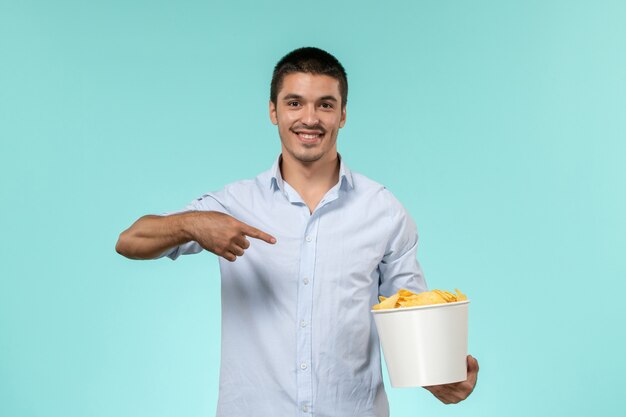 Front view young man holding basket with cips on blue wall film remote movie cinema theater