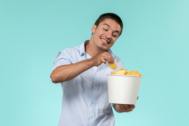 Front view young man holding basket with cips on blue wall film remote movies cinema theater