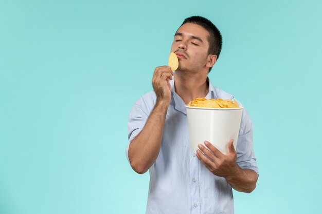 Вид спереди молодой человек, держащий корзину с чипсами на синей стене, удаленный кинотеатр