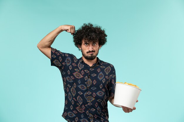 Front view young man holding basket with cips and flexing on the blue wall remote cinema film movies