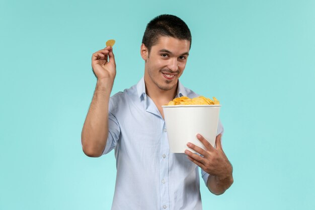 Вид спереди молодой человек, держащий корзину с чипсами на голубой стене, фильм удаленного кинотеатра мужчина