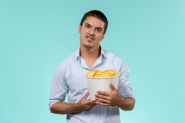 Front view young man holding basket with cips on light blue wall film remote movie cinema theater