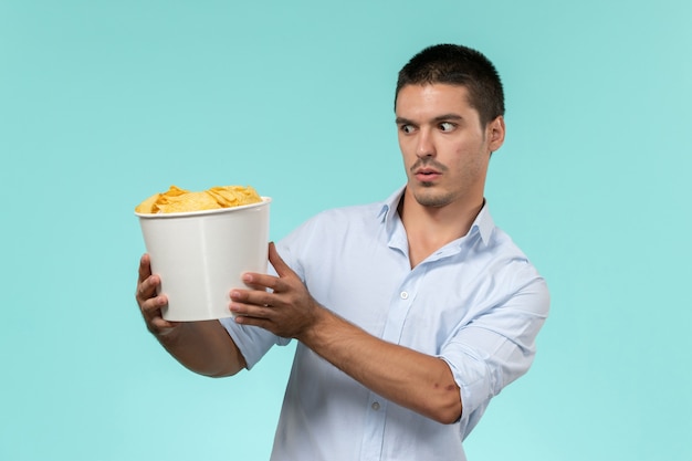 Cestino della holding del giovane di vista frontale con i cips sul teatro del cinema di film a distanza del film della parete blu chiaro