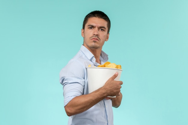 Front view young man holding basket with cips on light-blue wall remote movies cinema theater