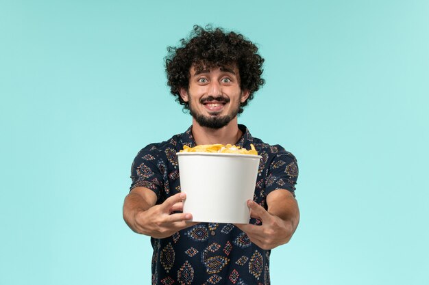 Front view young man holding basket with cips and smiling on a blue wall film cinema movie remote theater