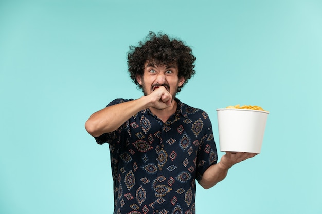 Free photo front view young man holding basket with potato cips on the blue desk remote film cinema movies theater