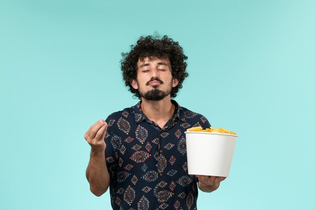 Front view young man holding basket with potato cips on blue desk remote male film cinema movies