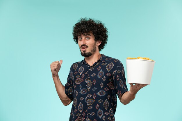 Вид спереди молодой человек, держащий корзину с картофельными чипсами на синем столе, удаленный кинотеатр, кинотеатр