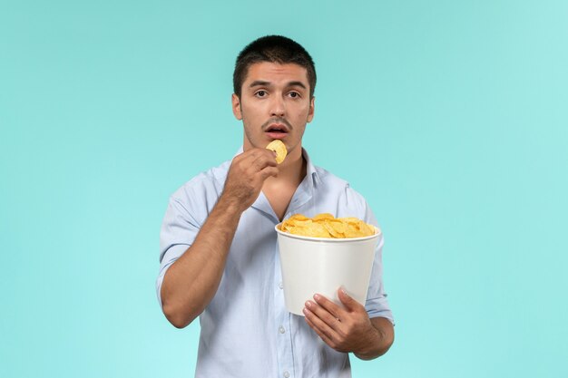 Front view young man holding basket with potato cips on a blue wall film remote movies cinema