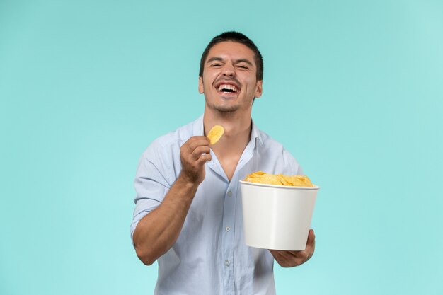 Front view young man holding basket with potato cips on blue wall film remote movies cinema