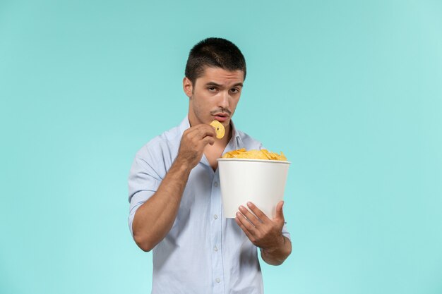 Вид спереди молодой человек, держащий корзину с картофельными чипсами на синей стене, удаленный кинотеатр