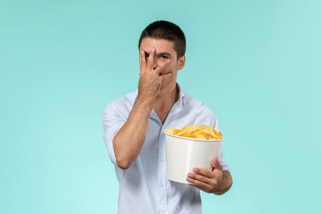 Вид спереди молодой человек, держащий корзину с картофельными чипсами на синей стене одинокий удаленный мужской кинотеатр