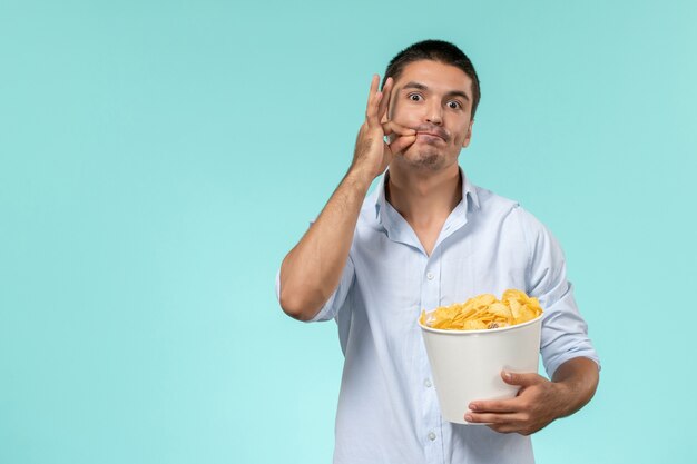 Front view young man holding basket with potato cips on blue wall remote movie cinema lonely male