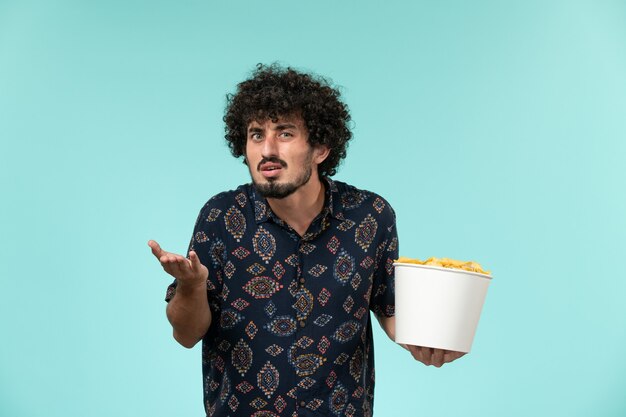 Вид спереди молодой человек, держащий корзину с картофельными чипсами на синей стене удаленного кинотеатра