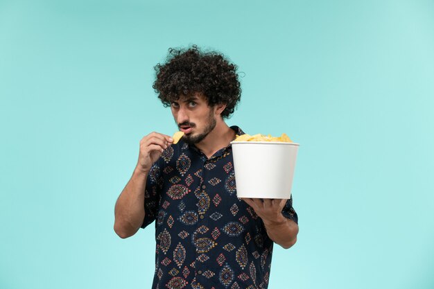 Foto gratuita giovane di vista frontale che tiene il canestro con le patatine fritte e che mangia sul maschio blu del teatro di film del cinema della parete