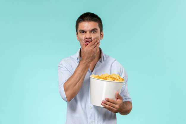Вид спереди молодой человек, держащий корзину с картофельными чипсами на голубой стене одинокий удаленный мужской кинотеатр