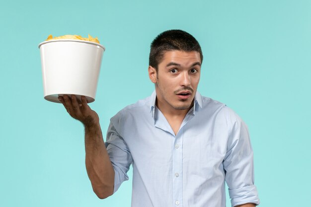 Вид спереди молодой человек, держащий корзину с картофельными чипсами на голубой стене удаленного кинотеатра одинокий мужчина