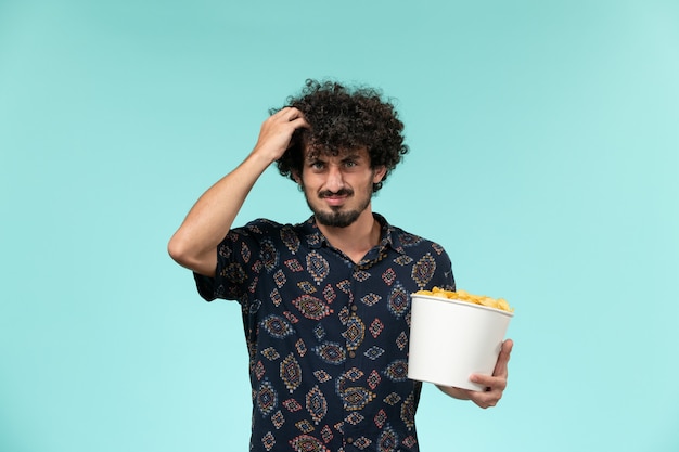 Front view young man holding basket with potato cips and watching movie on a blue wall male film cinema movies remote