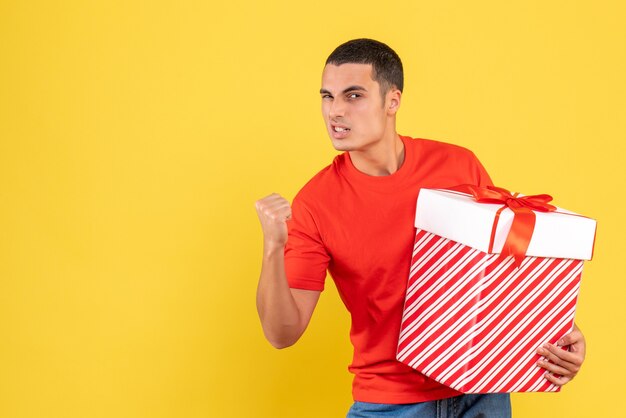 Front view of young man holding big christmas present on yellow wall