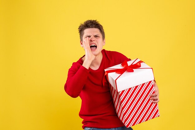 Front view of young man holding big christmas present on yellow wall