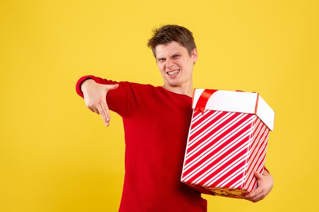 黄色の壁に大きなクリスマスプレゼントを保持している若い男の正面図
