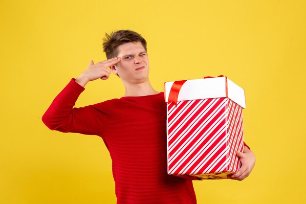 Front view of young man holding big christmas present on yellow wall