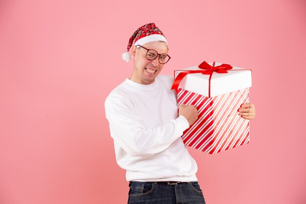 ピンクの壁に大きなプレゼントを保持している若い男の正面図