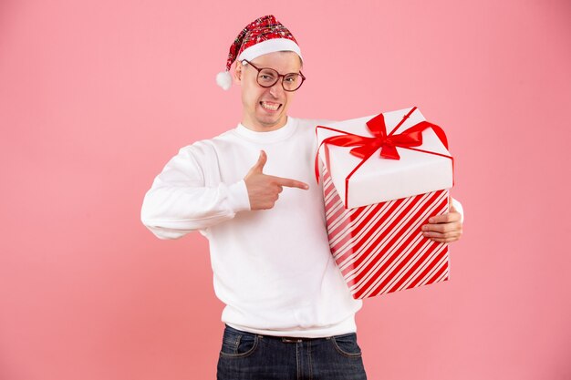 Front view of young man holding big present on a pink wall