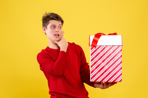 Front view of young man holding big xmas present on yellow wall