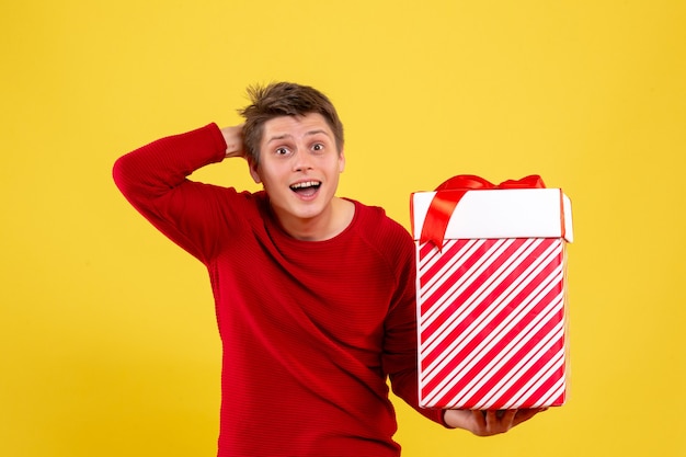 Front view of young man holding big xmas present on yellow wall