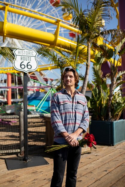 Front view of young man holding bouquet of roses at the amusement park