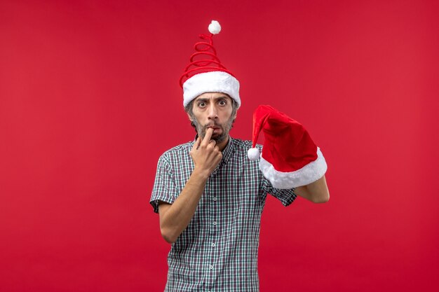 Front view of young man holding christmas cap on red wall