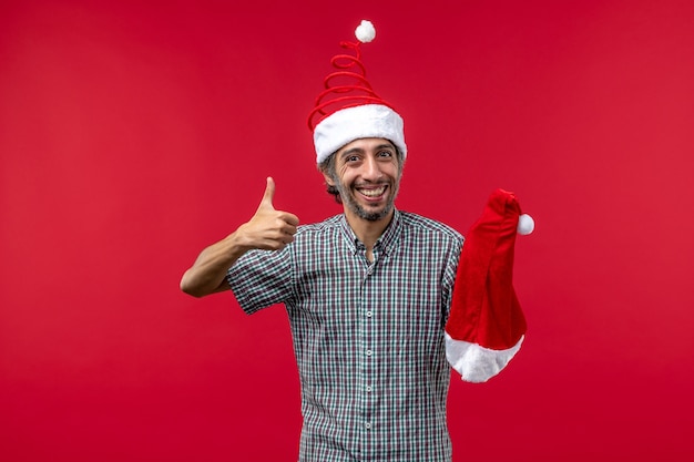 赤い壁にクリスマスの帽子を保持している若い男の正面図