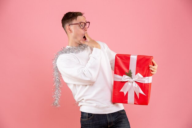 Front view of young man holding christmas present on pink wall