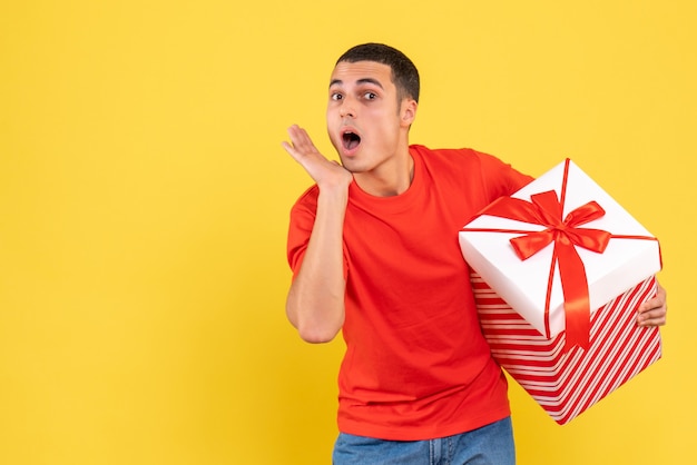 Front view of young man holding christmas present on a yellow wall