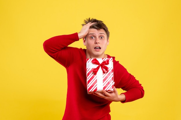 Front view of young man holding christmas present on the yellow wall